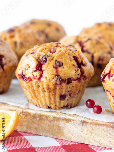 Cranberry orange muffin on a wooden table with white background. Vertical shot, a closeup. Freshly baked vegan muffins with cranberries and orange juice. Sweet vegan breakfast, dessert, or snack. 