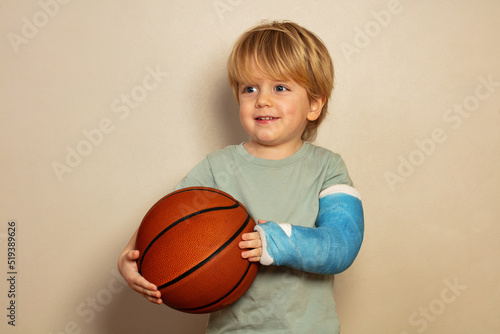 Boy hold basketball ball with broken hand in plaster cast