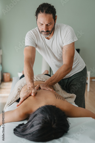 vertical photo of a masseur giving a massage to a patient lying on a massage table.