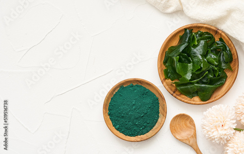 top view or flat lay laminaria or kelp seaweed and spirulina powder in wood plate and spoon background. spirulina powder with konbu and alga food on white table background. 