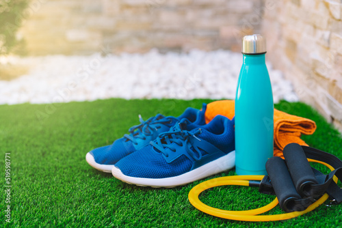 Close-up of objects and accessories for practising sport in a green grass garden. rubber bands for stretching, towel, water bottle. concept of practising sport in the open air.