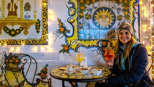 Tourist woman enjoying an aperitif in the historic city center of Taormina, Sicily, Italy, Europe, EU. Typical Italian Sicilian bar, restaurant. Beautiful mosaics with citrus fruits. Bam bar