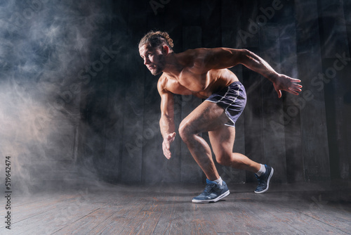 Strong athletic man sprinter ready to run. Professional athlete, runner training on dark background. Muscular, sportive male in dynamic movement. Concept of sport healthy lifestyle, fitness motivation