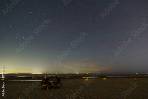 Two people stargazing and sitting on north sea beach under the night sky with constellation of the big dipper