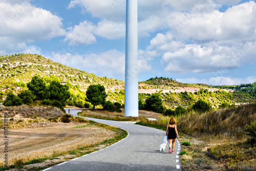 Curly-haired blonde woman walking with her puppy through the Rubió windmill park, La Anoia.