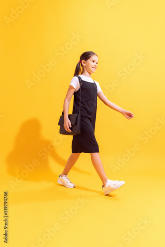 Pretty schoolgirl, kid wearing modern school uniform isolated on yellow background. Concept of emotions, fashion, beauty, studying, education