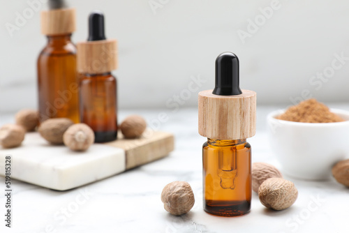 Bottles of nutmeg oil and nuts on white marble table, closeup. Space for text