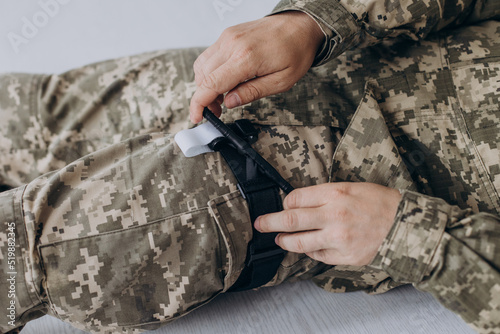 A military man demonstrates a combat medical tourniquet to stop blood during first aid. Instructions for combat tactical equipment.