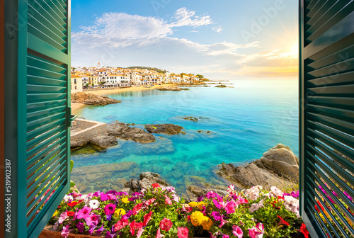 View through an open window with shutters of the whitewashed Costa Brava village of Calella de Palafrugell, Spain, as the sun sets on the Catalonian coast of Southern Spain.