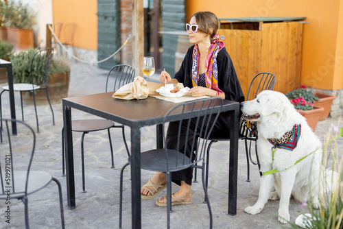 Woman tasting cheese and wine sitting with her dog at local farm shop in Maremma region of Italy. Concept of italian cuisine and local farming. Italian shepherd dog from this region
