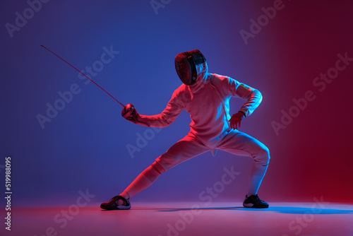 Male fencer with smallsword practicing fencing isolated on purple background in neon light. Sport, energy, skills, achievements