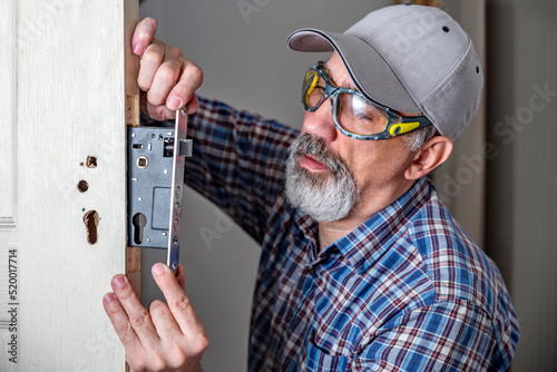 Door lock installation, repair, or replacement service. Door hardware installer locksmith working with open white door indoor