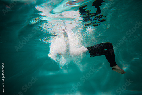 Beautiful underwater shooting, guy in white shirt and pants has fallen under the water and drowning. go to bottom, concept. young man paddles with his hands under water, waves and splashes around him