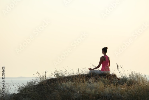 Woman meditating on hill near sea, back view. Space for text