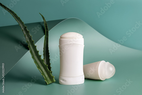 Roll on antiperspirant and solid deodorant near two fresh aloe leaves against teal blue wavy baskground. Natural herbal toiletries and organic cosmetics for body care.