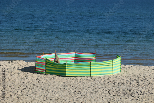 Parasol słoneczny na plaży nadmorskiej w wakacje razem z parawanem na wiatr. 