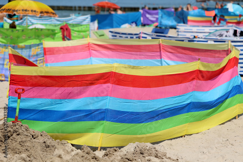 Parasol słoneczny na plaży nadmorskiej w wakacje razem z parawanem na wiatr. 