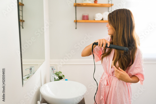 Mexican young woman straightening her hair with an iron