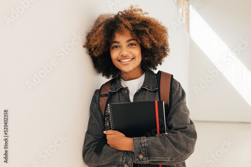 Portrait of a young beautiful female student leaning a wall. Smiling girl looking at camera while standing in high school.