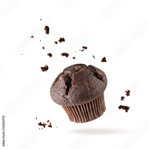 Fresh baked single chocolate muffin with crumbs flying on white background. Sweet dark cupcake falling.