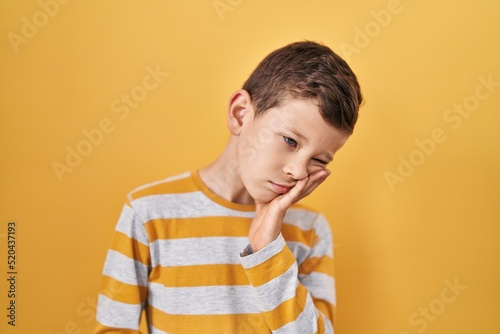 Young caucasian kid standing over yellow background thinking looking tired and bored with depression problems with crossed arms.