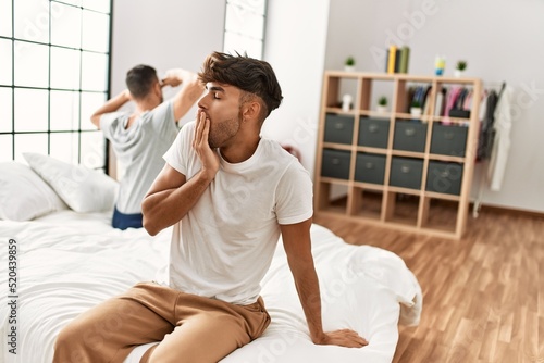 Two hispanic men couple waking up stretching arms and yawning at bedroom