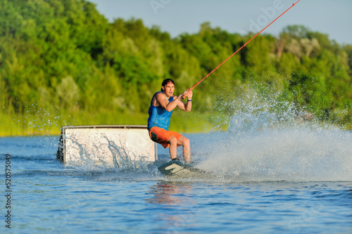 A professional wakeboarder rides on the lake in sunny weather, performing figures