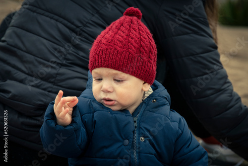 Niño bebé con gorro de lana rojo mirando sus manos con arena en la playa en otoño e invierno