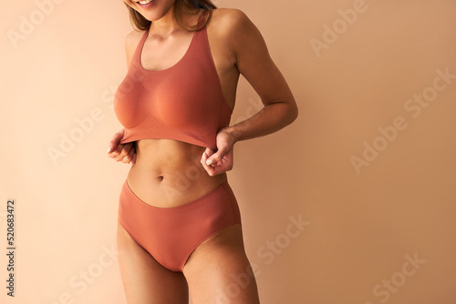  Cropped image of beautiful young woman posing in lingerie showing her bra on beige background.