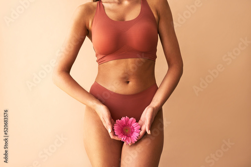 Cropped image of woman in lingerie holding pink flower on beige background. Women's health, cosmetology.