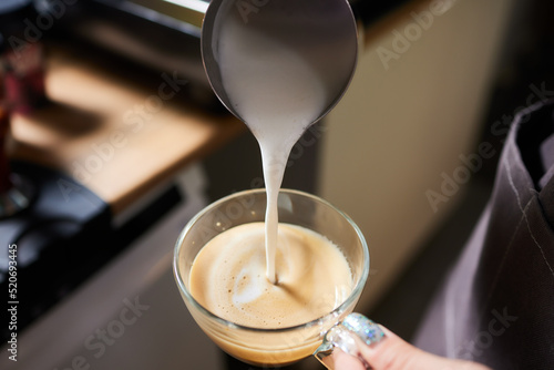 Top view shot of professional barista pouring milk from jar in to a cup of coffee, coffee being prepared by a barista. Focus on hands holding cup of coffee.