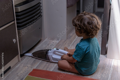 A sweet little boy vacuums the caravan while on vacation. A cute boy is cleaning the caravan.