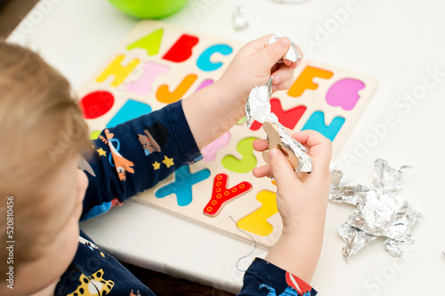 Two year boy playing with wooden alphabet letters board. Letters wrapped in foil. Intellectual game, preschool implement for early education. Verbal and memory training exercise.