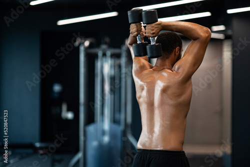 Shirtless Muscular Black Man Training With Two Dumbbells At Gym, Rear View