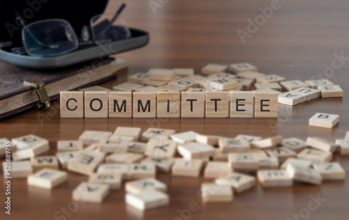 committee word or concept represented by wooden letter tiles on a wooden table with glasses and a book