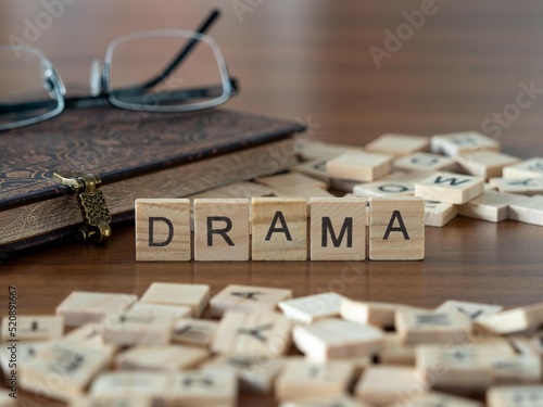 drama word or concept represented by wooden letter tiles on a wooden table with glasses and a book