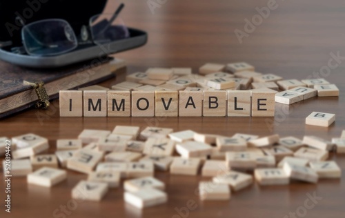 immovable word or concept represented by wooden letter tiles on a wooden table with glasses and a book