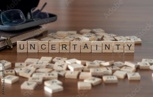 uncertainty word or concept represented by wooden letter tiles on a wooden table with glasses and a book