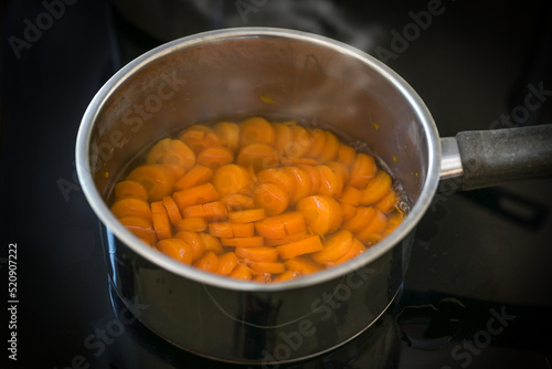 Slices of carrot are cooked in water in a steel pot on a black stove for a healthy digestible vegetable meal or soup against diarrhea, selected focus