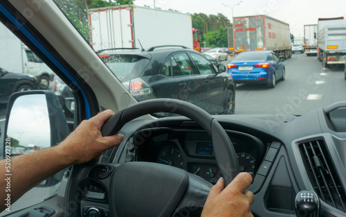 Male hands hold the steering wheel of a car while driving on a highway in a traffic jam.