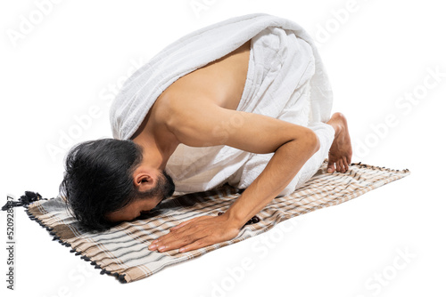 Man wearing ihram clothes praying with prayer rug while prostration on isolated background