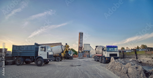 Concrete mixer trucks parked at plant yard, concrete mixing and batching factory, panoramic view. Concrete batching plant. Producing сoncrete and portland cement mortar for construction and formworks