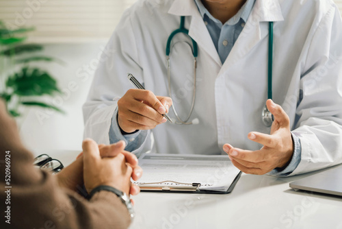 A professional physician in a white medical uniform talks to discuss results or symptoms and gives a recommendation to a male patient and signs a medical paper at an appointment visit in the clinic.