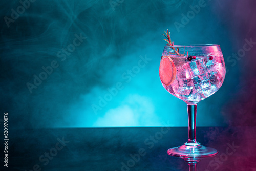 Cold gin tonic under pink and blue light illumination on smoky background with copy space.