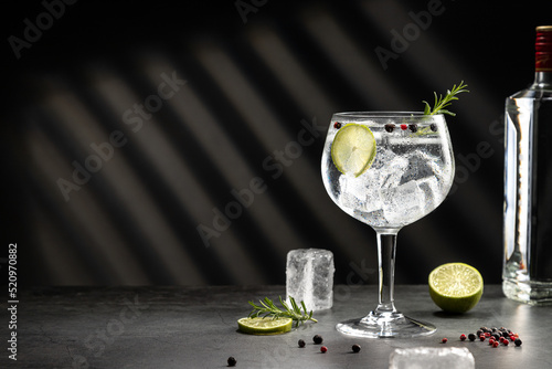 Cold glass of gin tonic with ice and hard shadows on dark gray background with copy space.