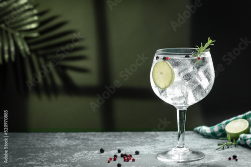 Gin tonic cocktail and shadows next to the window on dark concrete background.