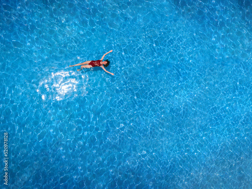 Aerial view of a swimming pool in summer. Young woman in a swimsuit swimming and refreshing.