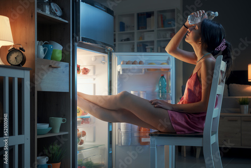 Woman cooling herself in front of the open fridge