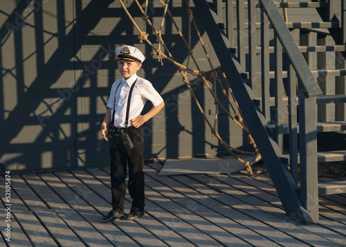 The little captain of the ship inspects the ship. Stands on the deck of a pirate ship. White shirt. wooden staircase. Rope marine decor.
