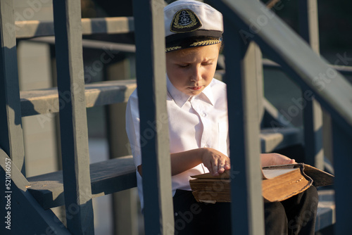The little captain of the ship inspects the ship. Stands on the deck of a pirate ship. White shirt. wooden staircase. Rope marine decor.
